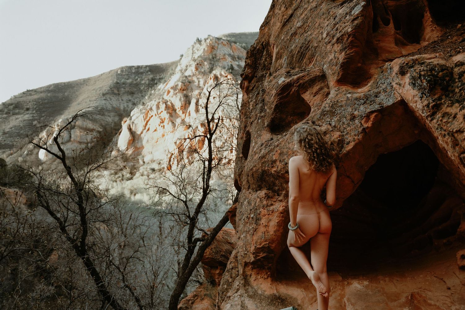 Woman looking off in distance posing for outdoor boudoir photo shoot with red rock cliffs in background.