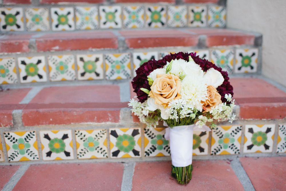 A wedding bouquet with peach and white roses rests on decorative tiled steps with colorful geometric patterns.
