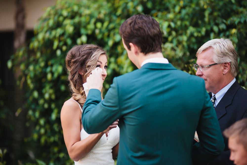 Wedding party members in green suits gather for photos in a lush garden setting.