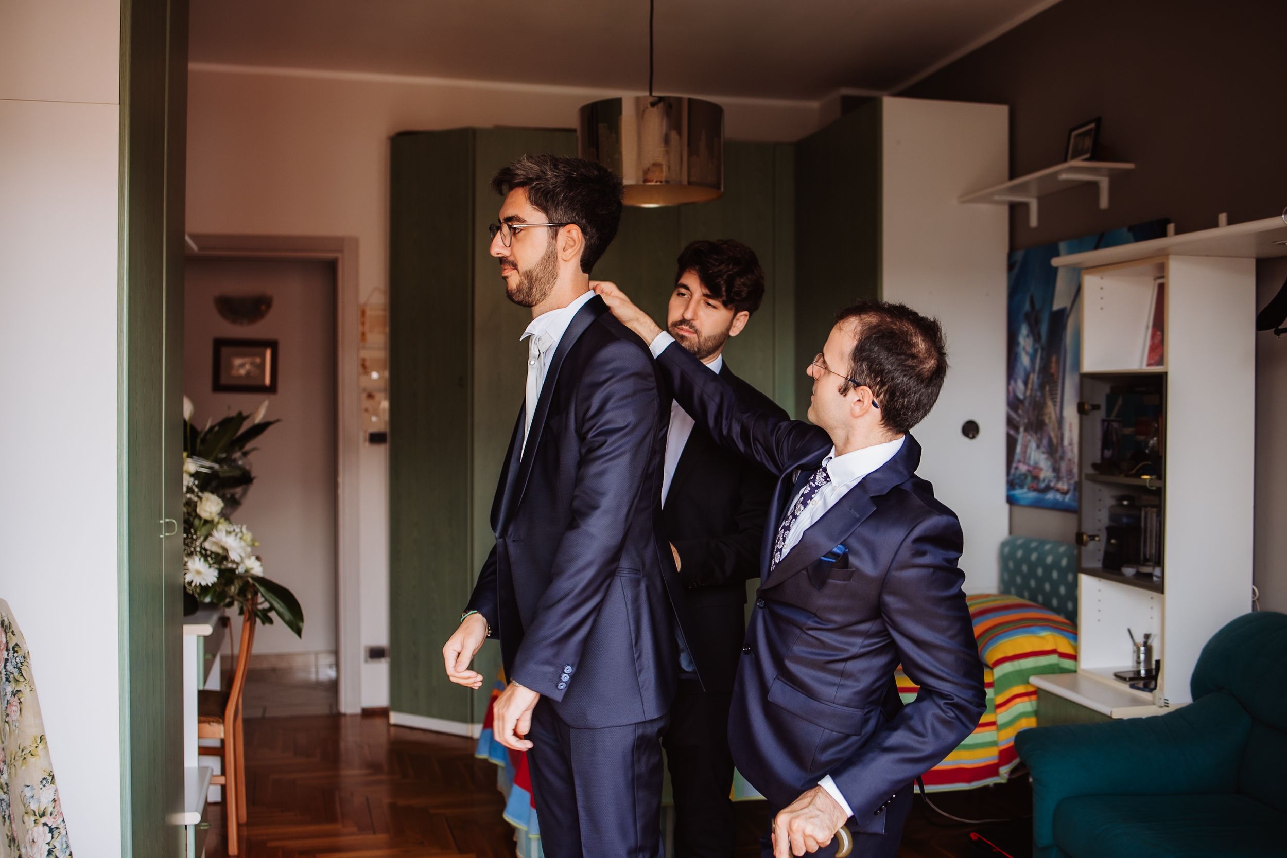 Two men in suits stand together in a room having a conversation.