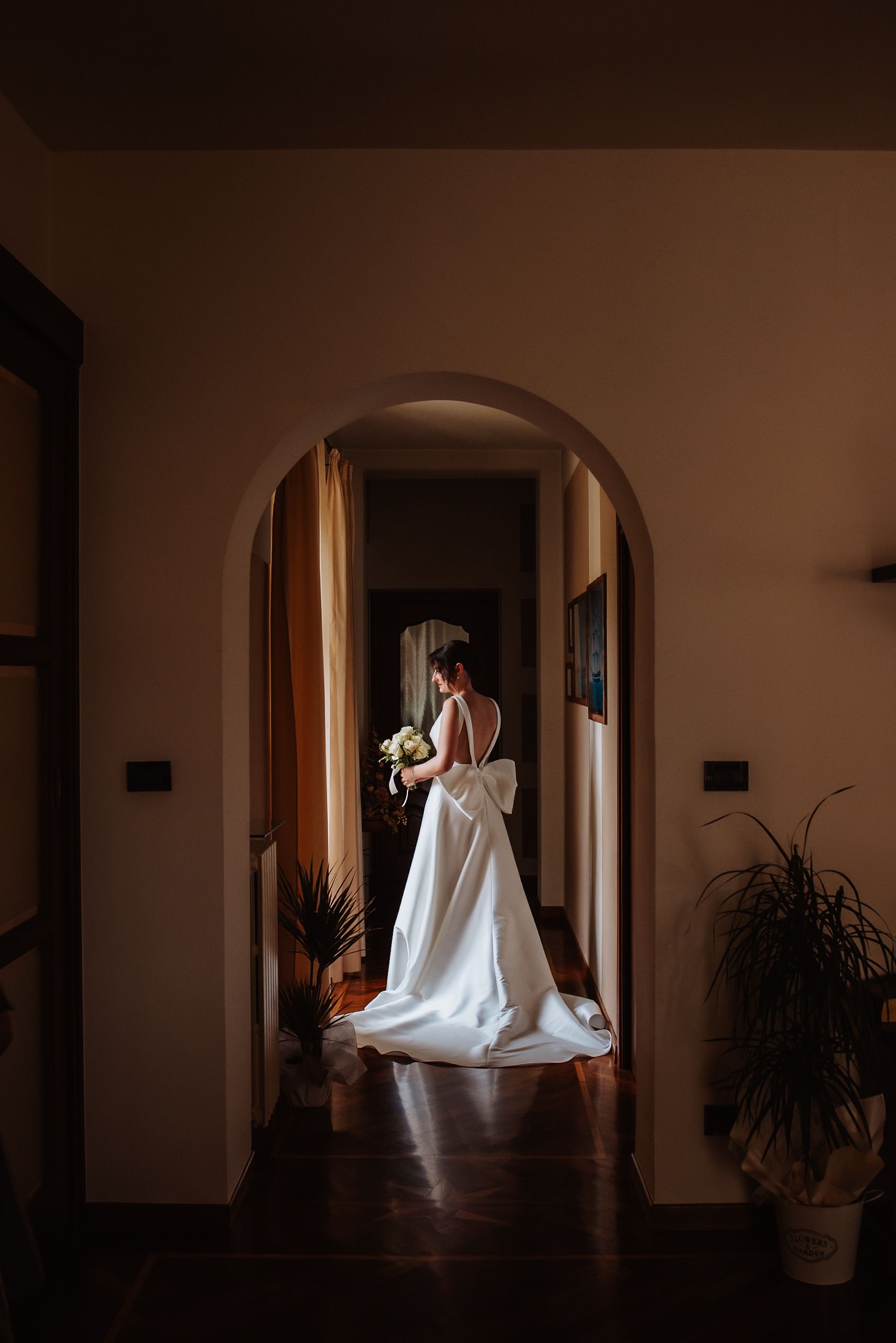 Dramatic silhouette of a bride in a flowing white gown walking through arched doorways in a dark hallway.