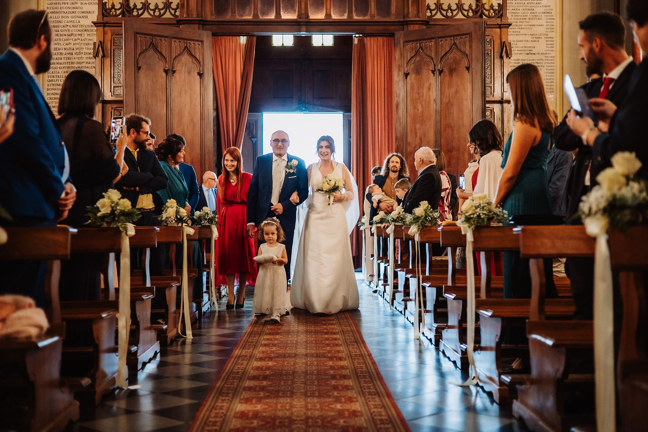 Wedding ceremony in a grand church sanctuary with guests seated in wooden pews and sunlight streaming through windows.