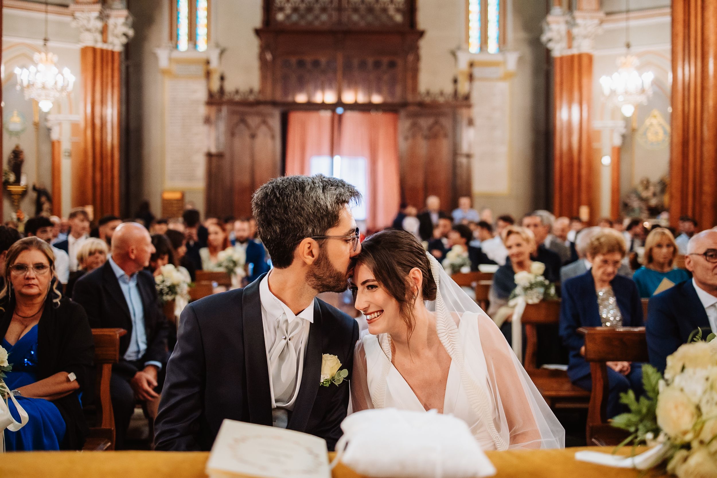 Wedding guests gather in an ornate ballroom with chandeliers and elegant decor during an indoor ceremony.