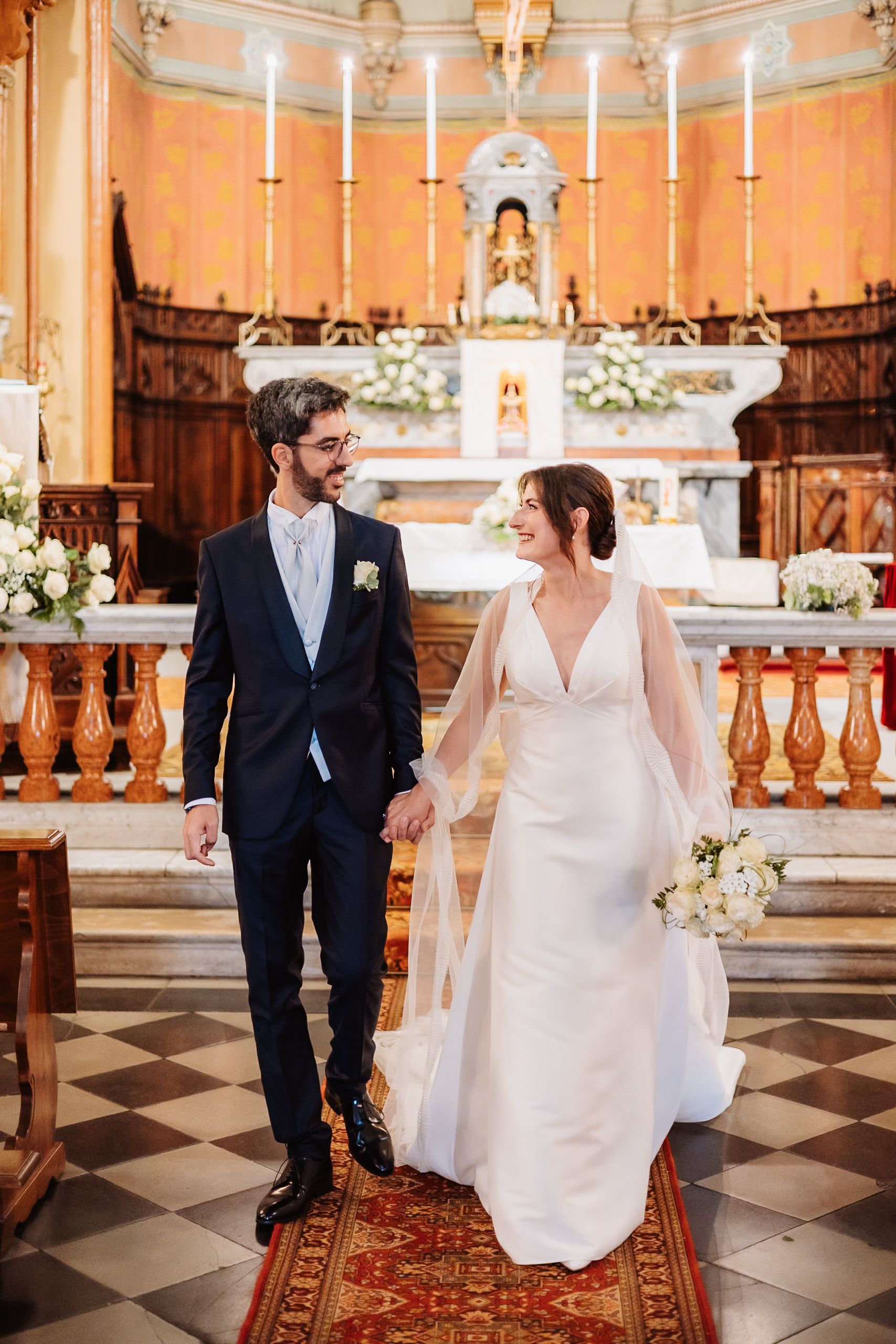 A couple shares intimate moments in a beautiful church with checkered floors and ornate altar during their wedding ceremony.