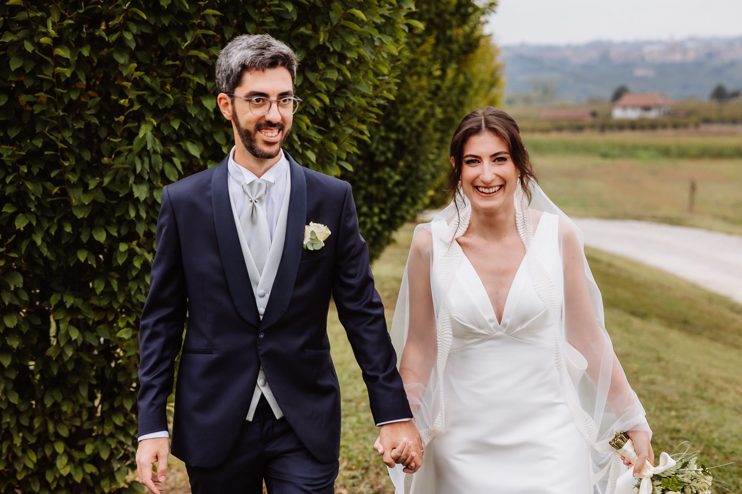 Newlywed couple walking hand in hand through a scenic countryside landscape on their wedding day.