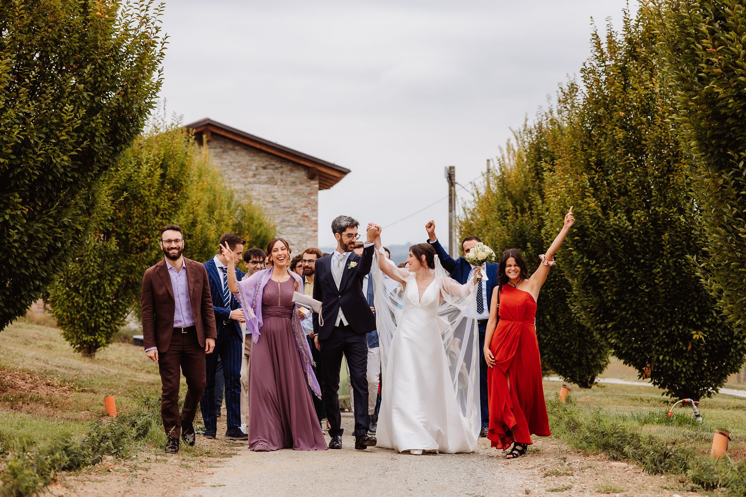 Wedding party walks along a tree-lined path during an autumn outdoor celebration.