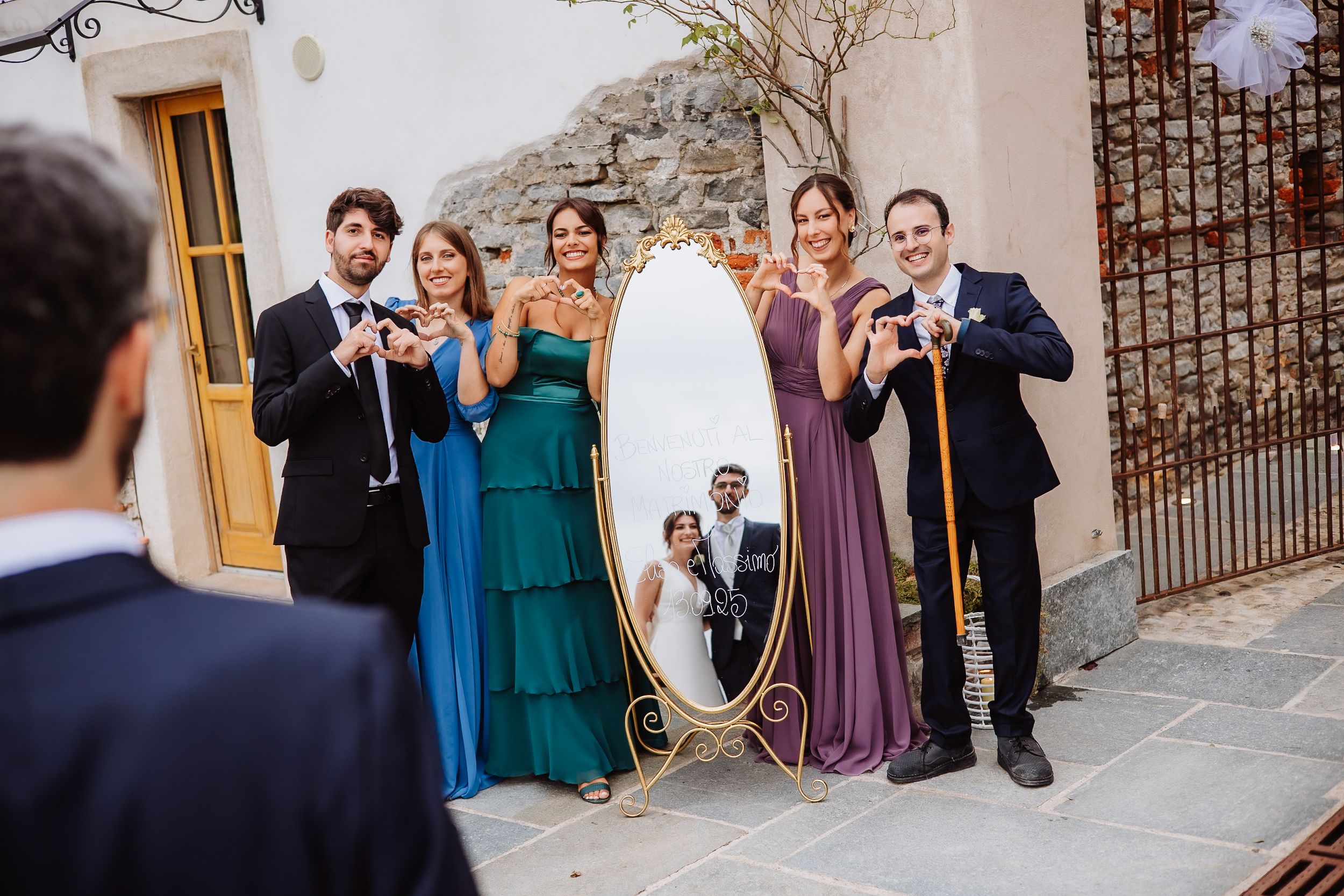Wedding party in teal and purple dresses pose together on stone steps outside historic building.