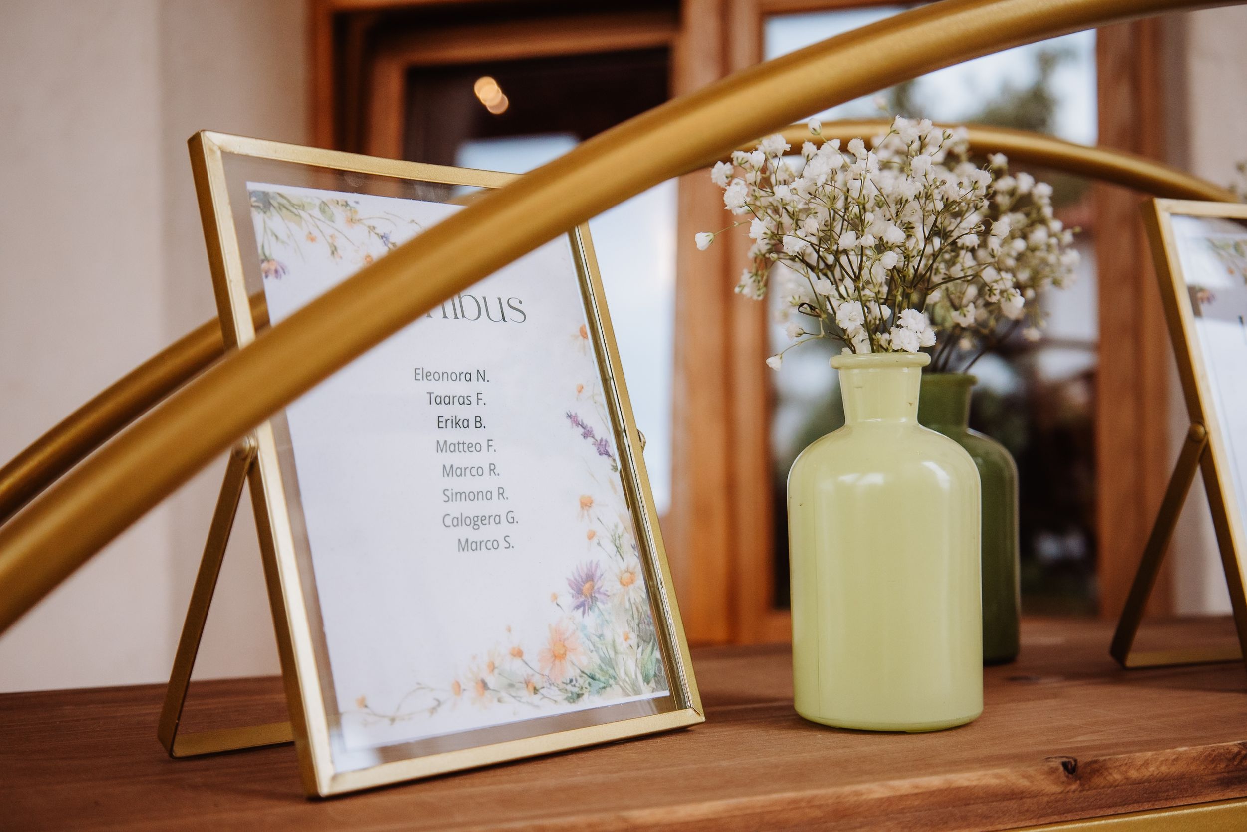 Decorative glass vase and framed signage displayed on wooden table at wedding reception venue.