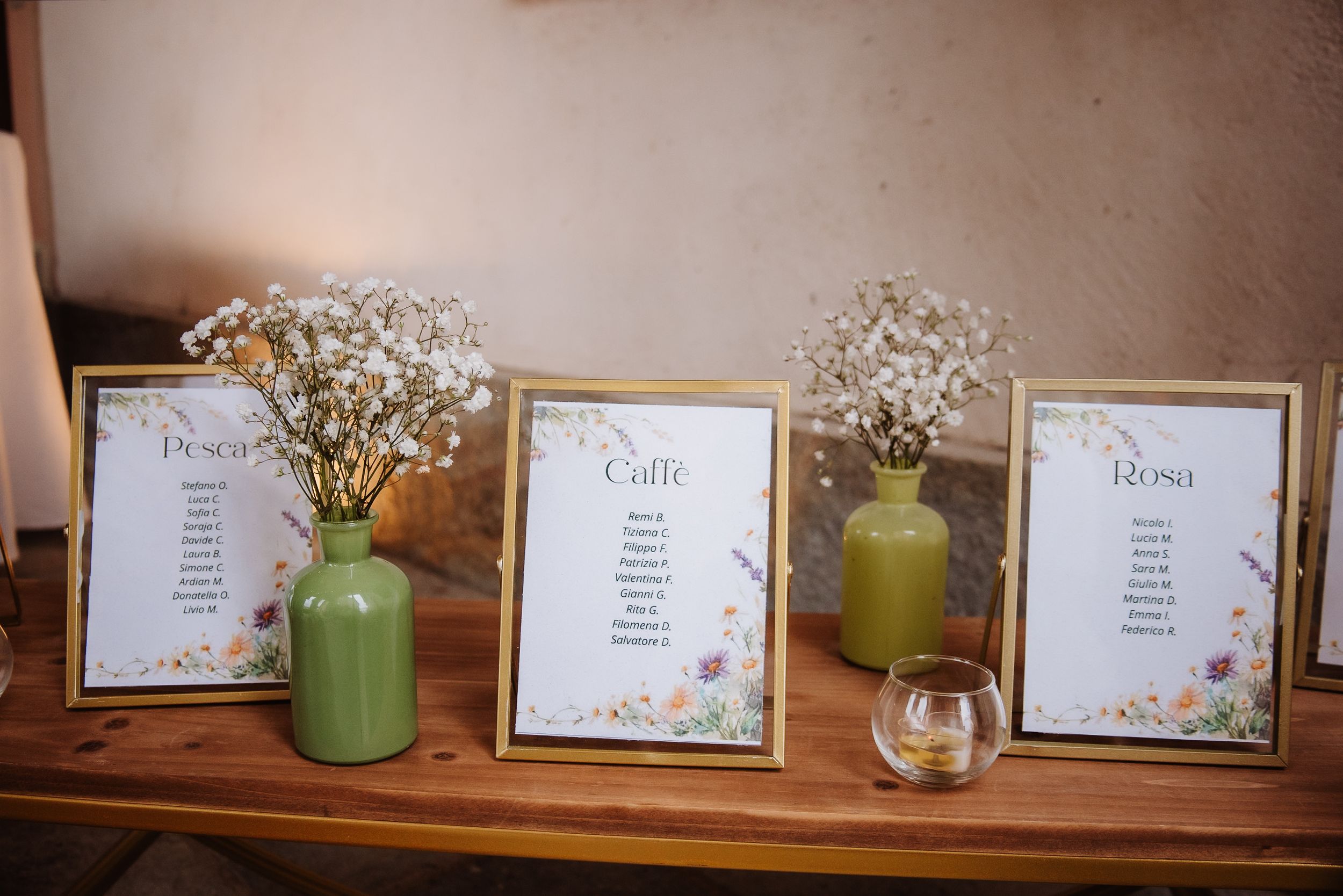 A row of decorative mason jars with white flowers and name cards displayed on a wooden shelf against a warm wall.