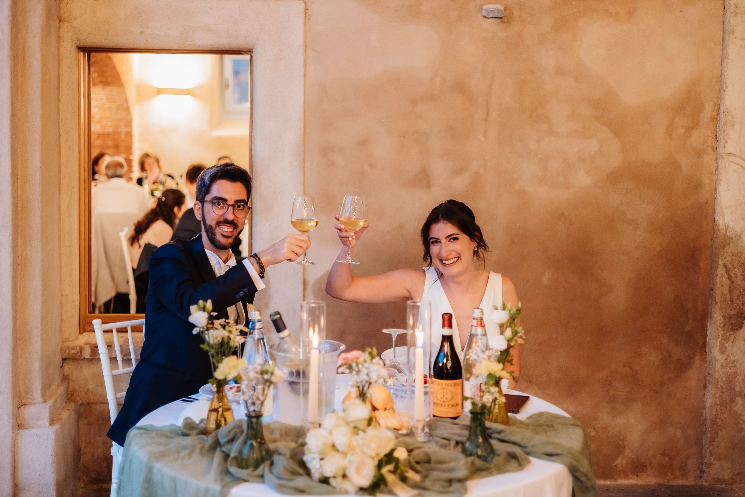 Newlyweds celebrate joyfully at their reception table decorated with elegant floral centerpieces and champagne.