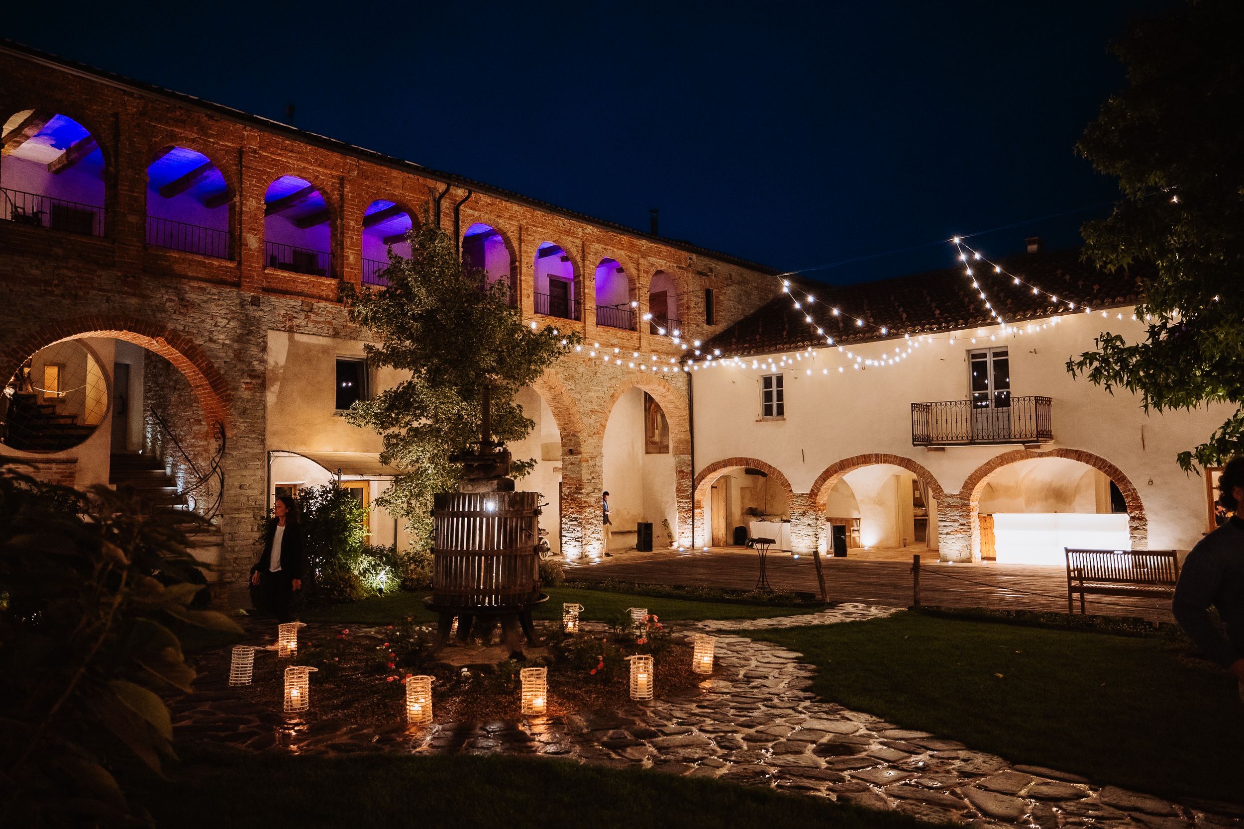 Illuminated stone courtyard with arched walkways and string lights creating a romantic evening ambiance at a historic venue.
