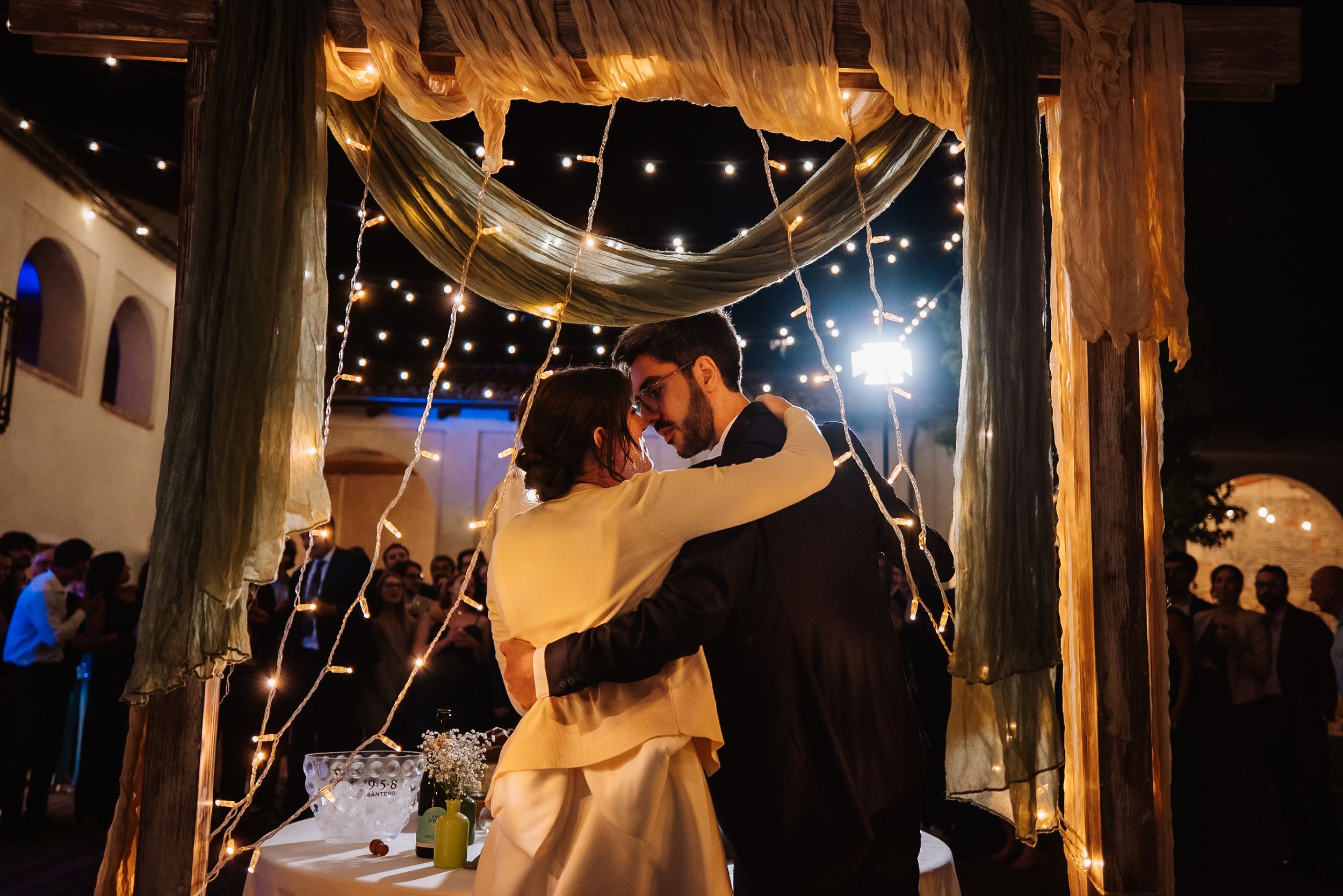 String lights illuminate a rustic barn wedding reception with draped fabric decor and romantic ambiance.