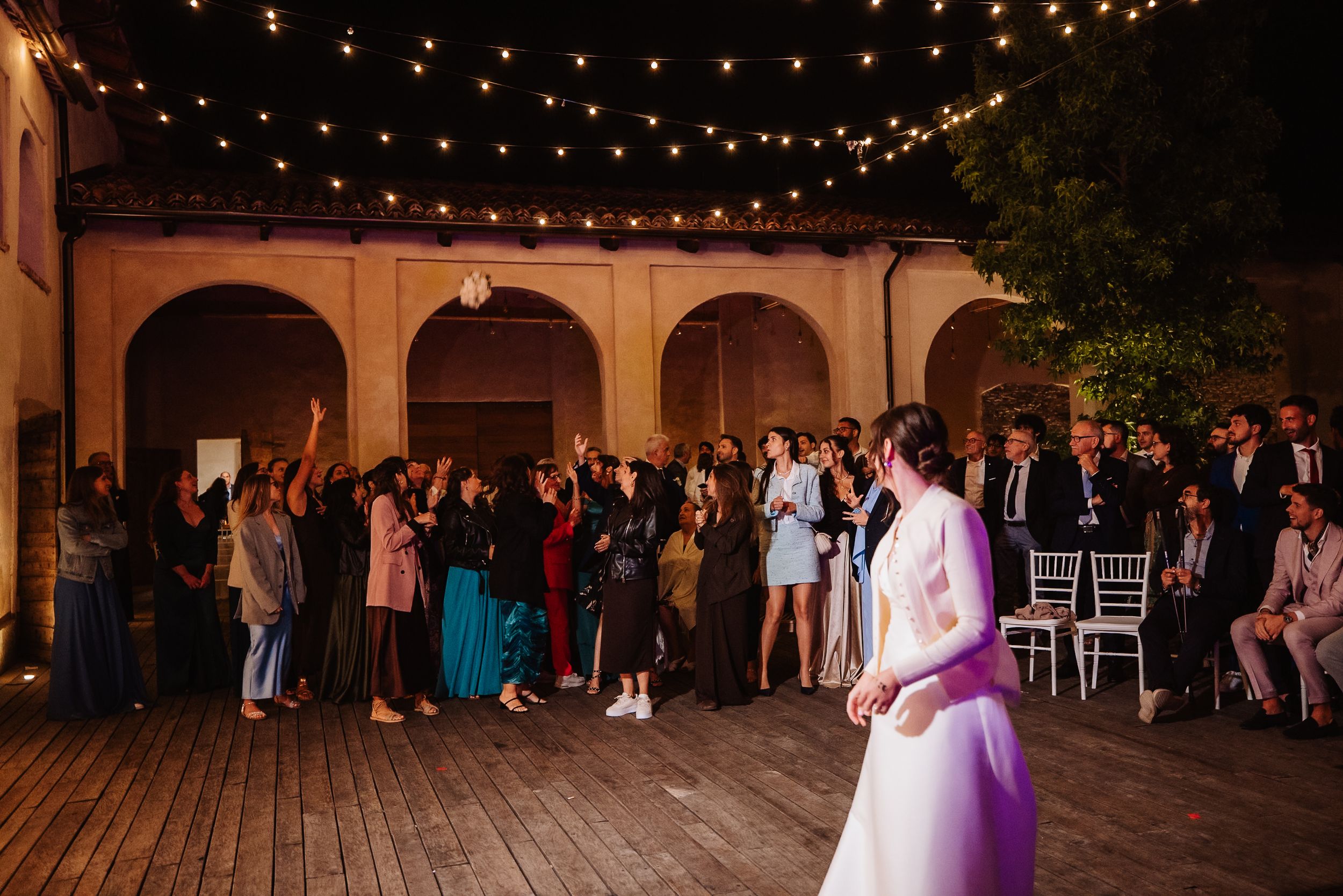 String lights illuminate an outdoor wedding reception venue with guests mingling in the background.