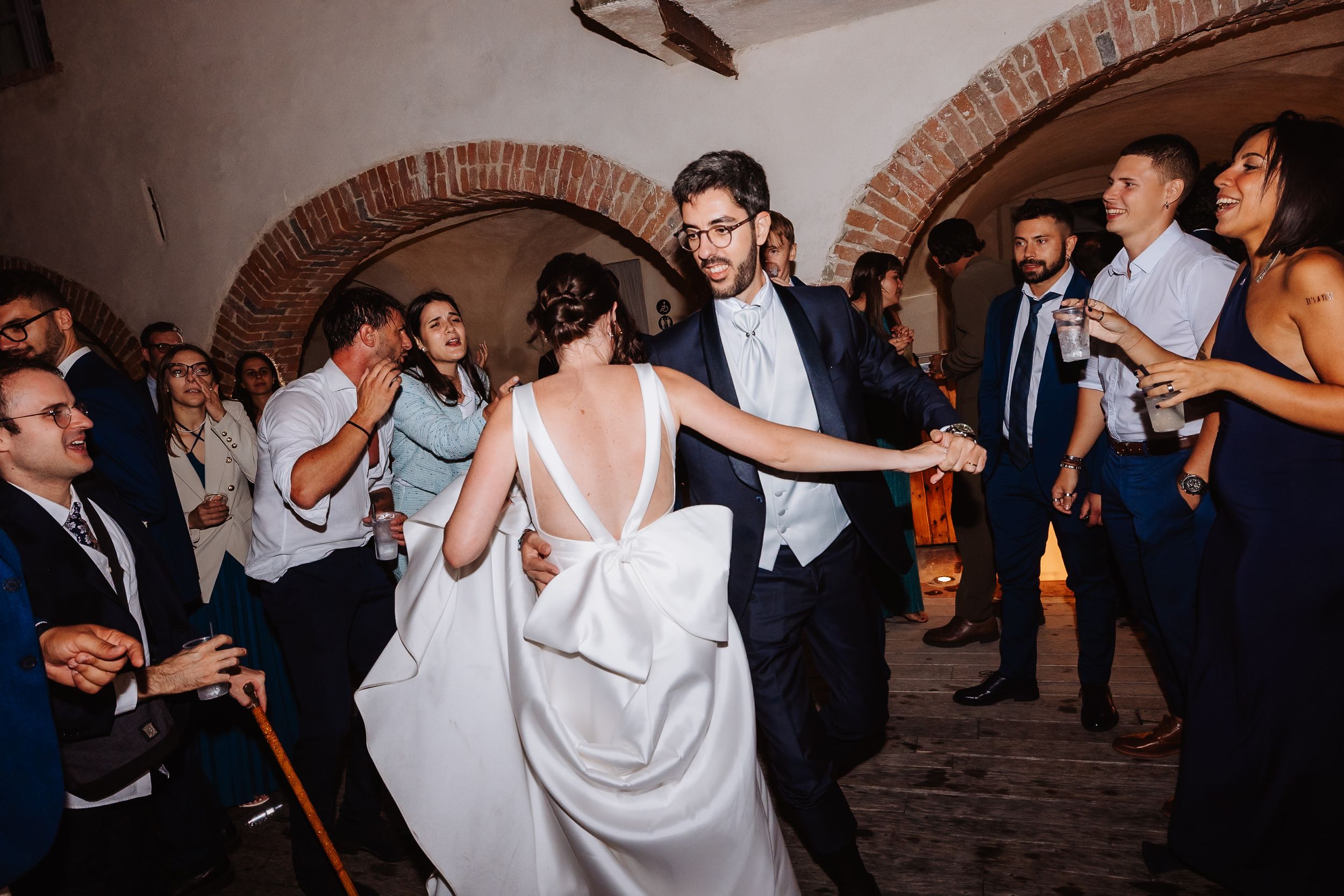Guests enjoying themselves and dancing under brick archways at an indoor wedding celebration.
