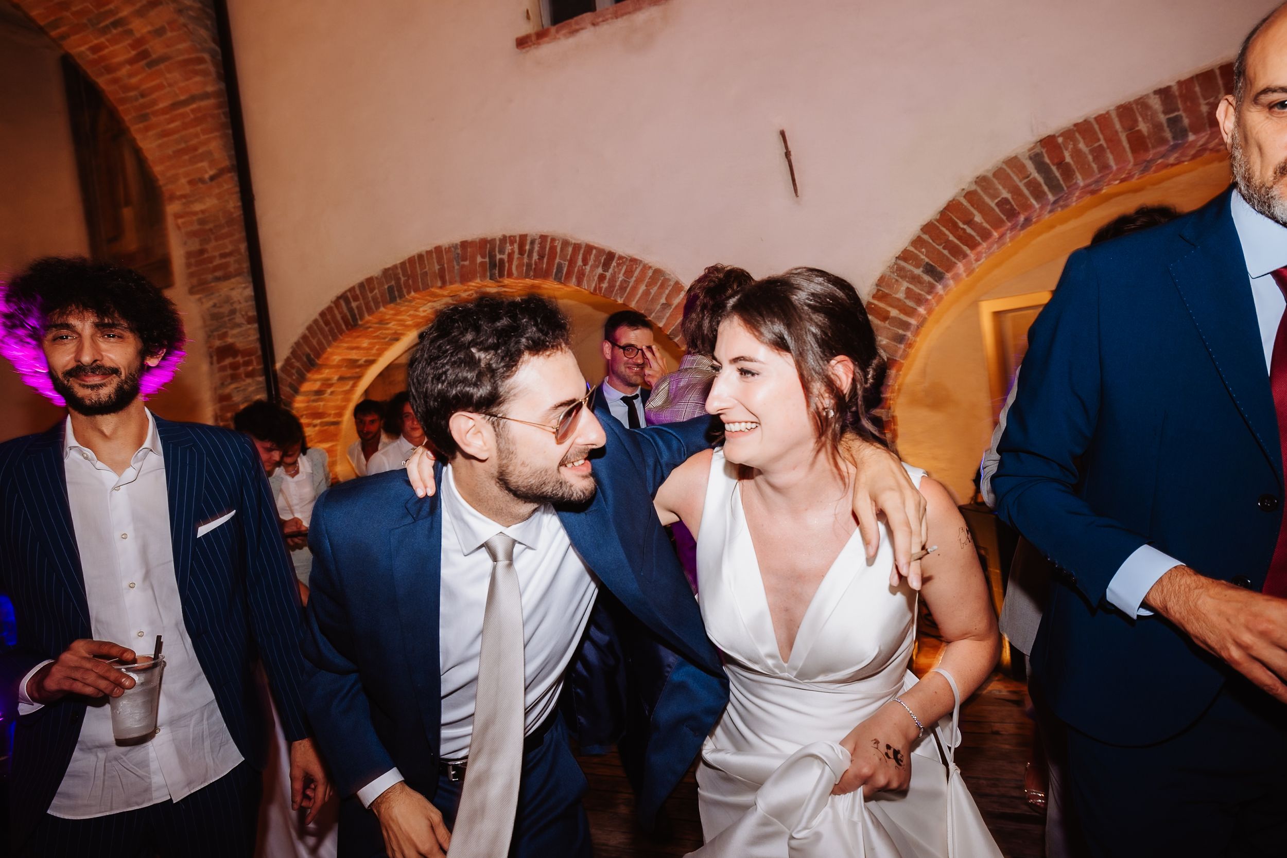 Couple dances energetically at a wedding reception under rustic brick archways.