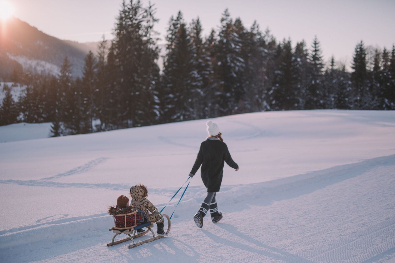 Person pulling a sled through snowy winter landscape at sunset.