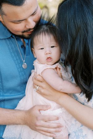 A series of tender moments showing a baby in a pink dress being held and comforted by adults in blue shirts.