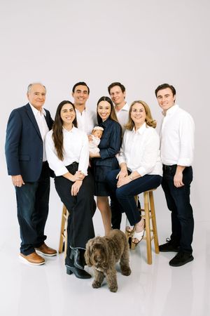 A family in coordinated black and white outfits poses with their brown dog in a modern studio setting.