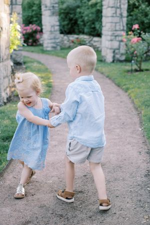 A toddler in light blue clothing plays and laughs while walking along a stone-lined garden path.