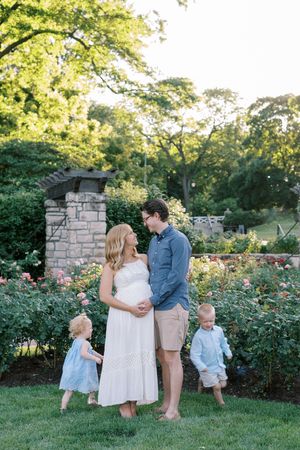 A family shares tender moments together in a lush garden setting with blooming roses and stone walls at sunset.