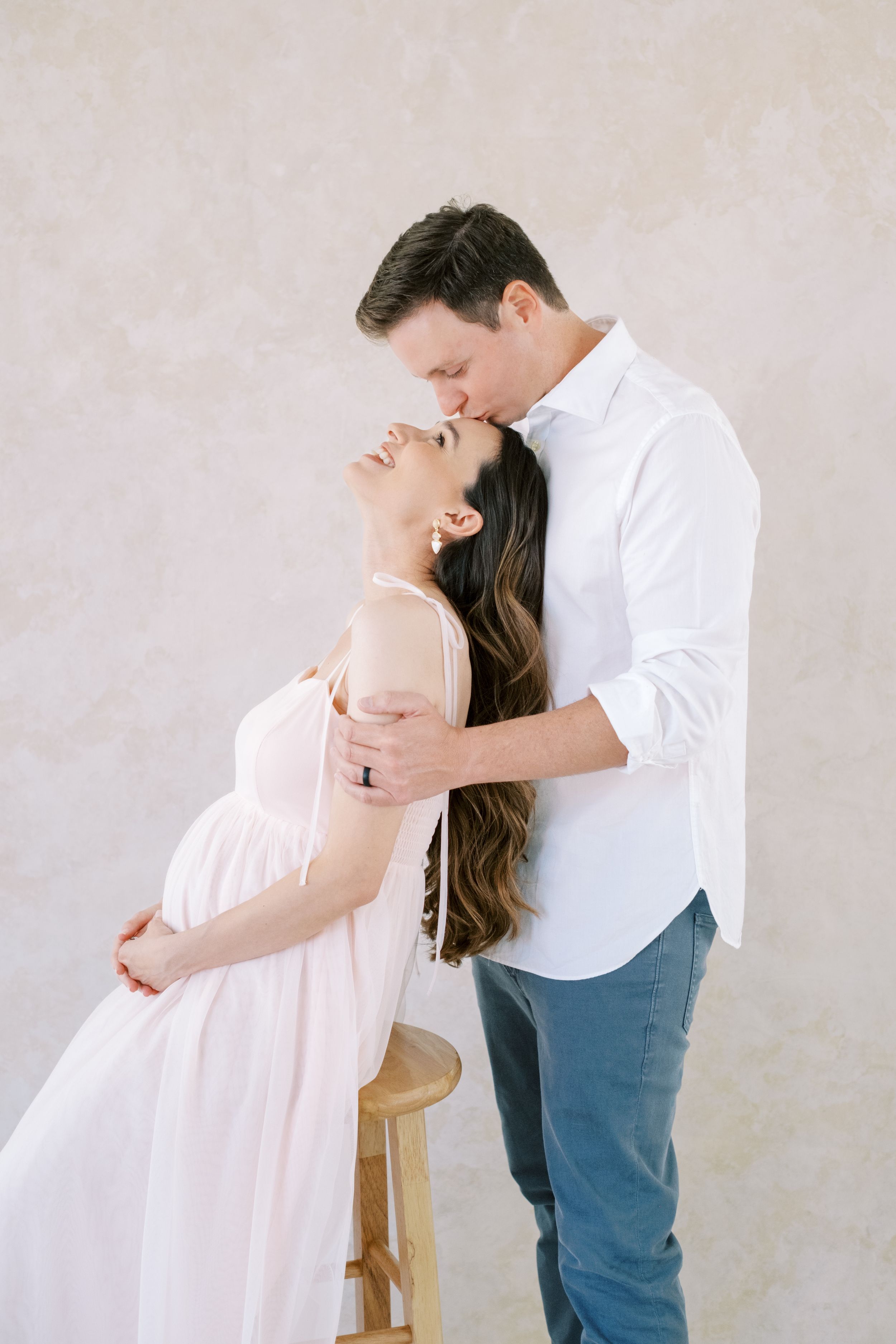 A couple in soft lighting shares an intimate dance-like pose against a neutral backdrop.