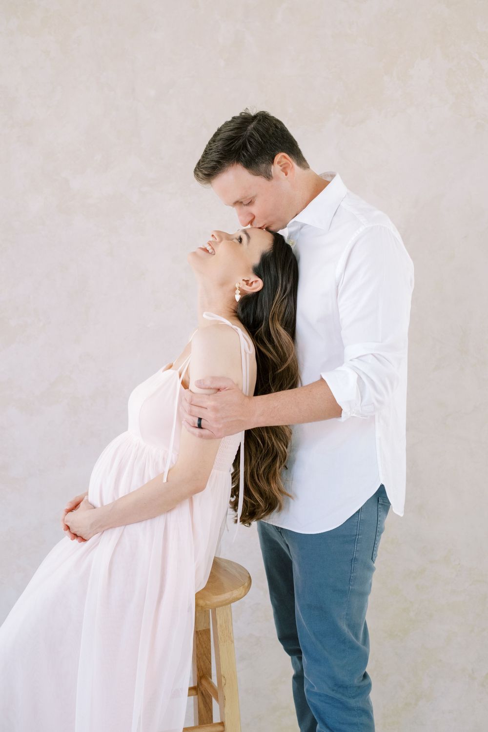 A couple in soft lighting shares an intimate dance-like pose against a neutral backdrop.