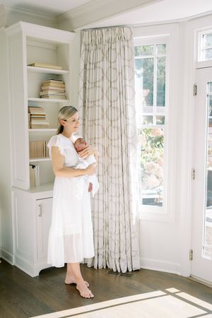 A bright white nursery corner with built-in shelves, floral curtains, and natural sunlight streaming through French doors.