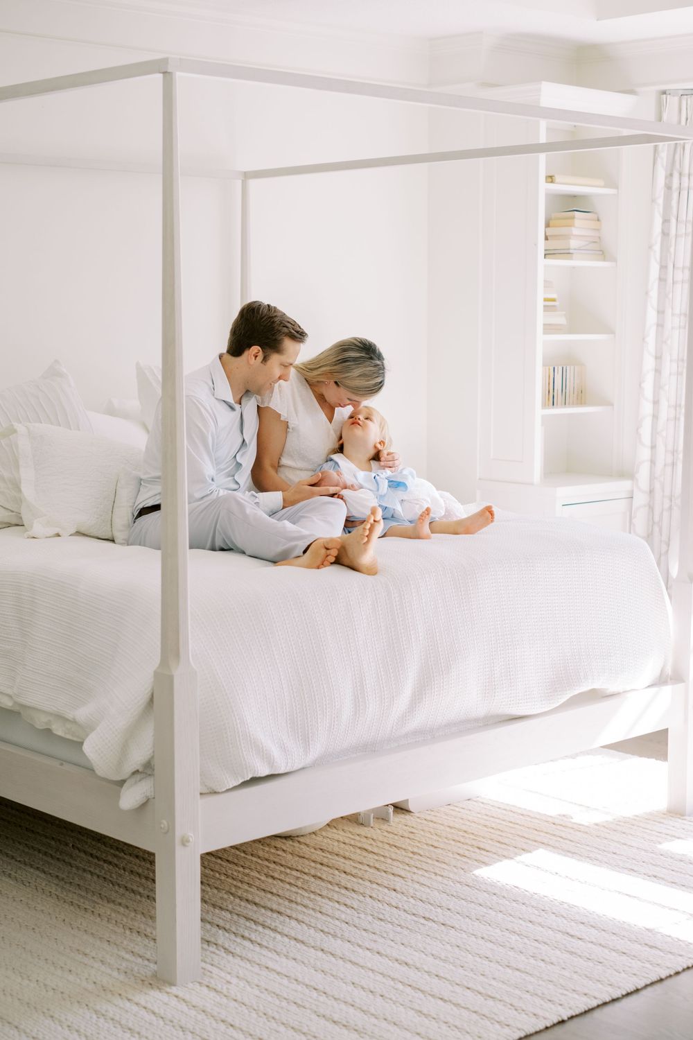 Two people lying in a white canopy bed with natural light streaming through windows.