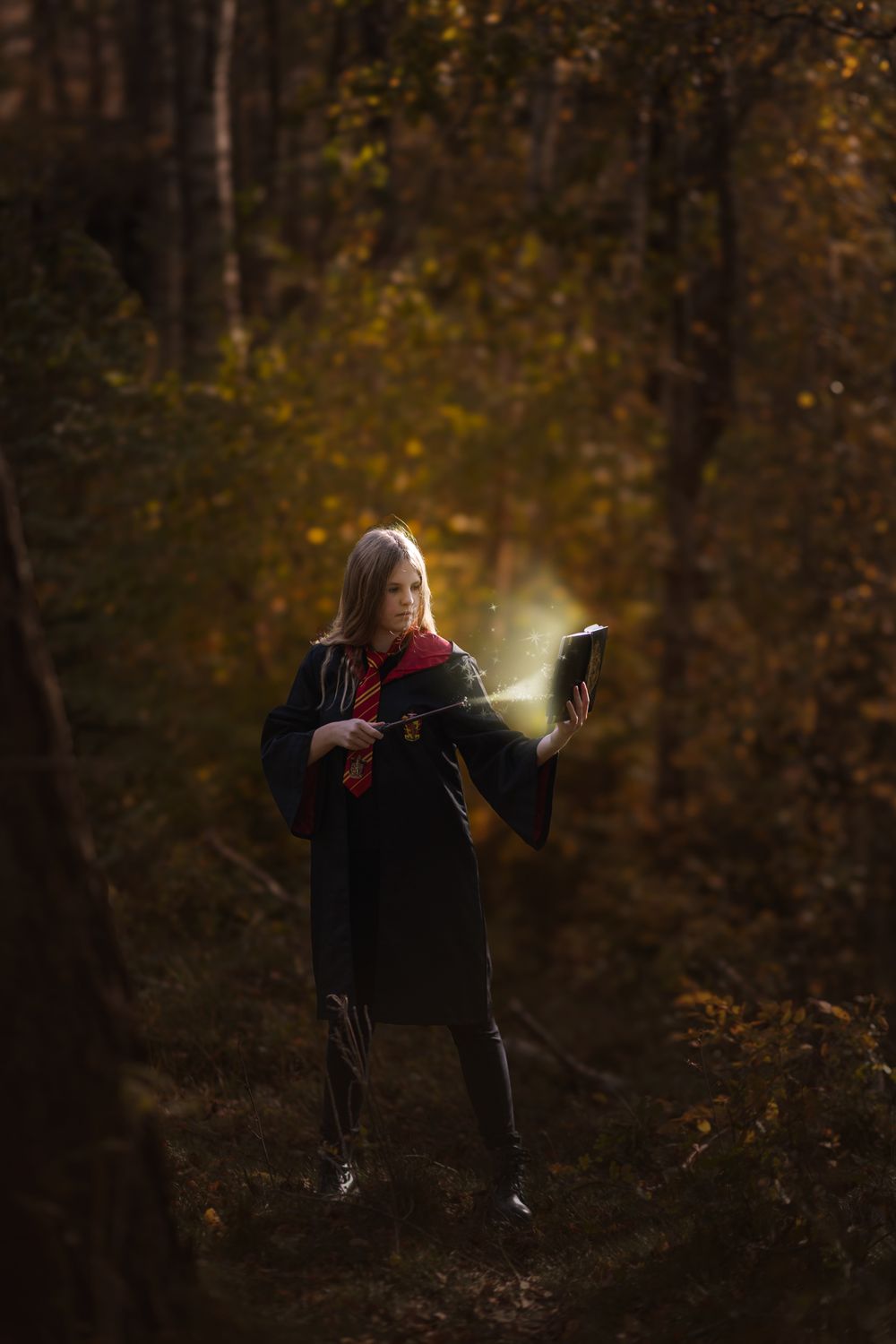 A figure sits in a dark forest surrounded by autumn foliage while holding a glowing light source in their hands.