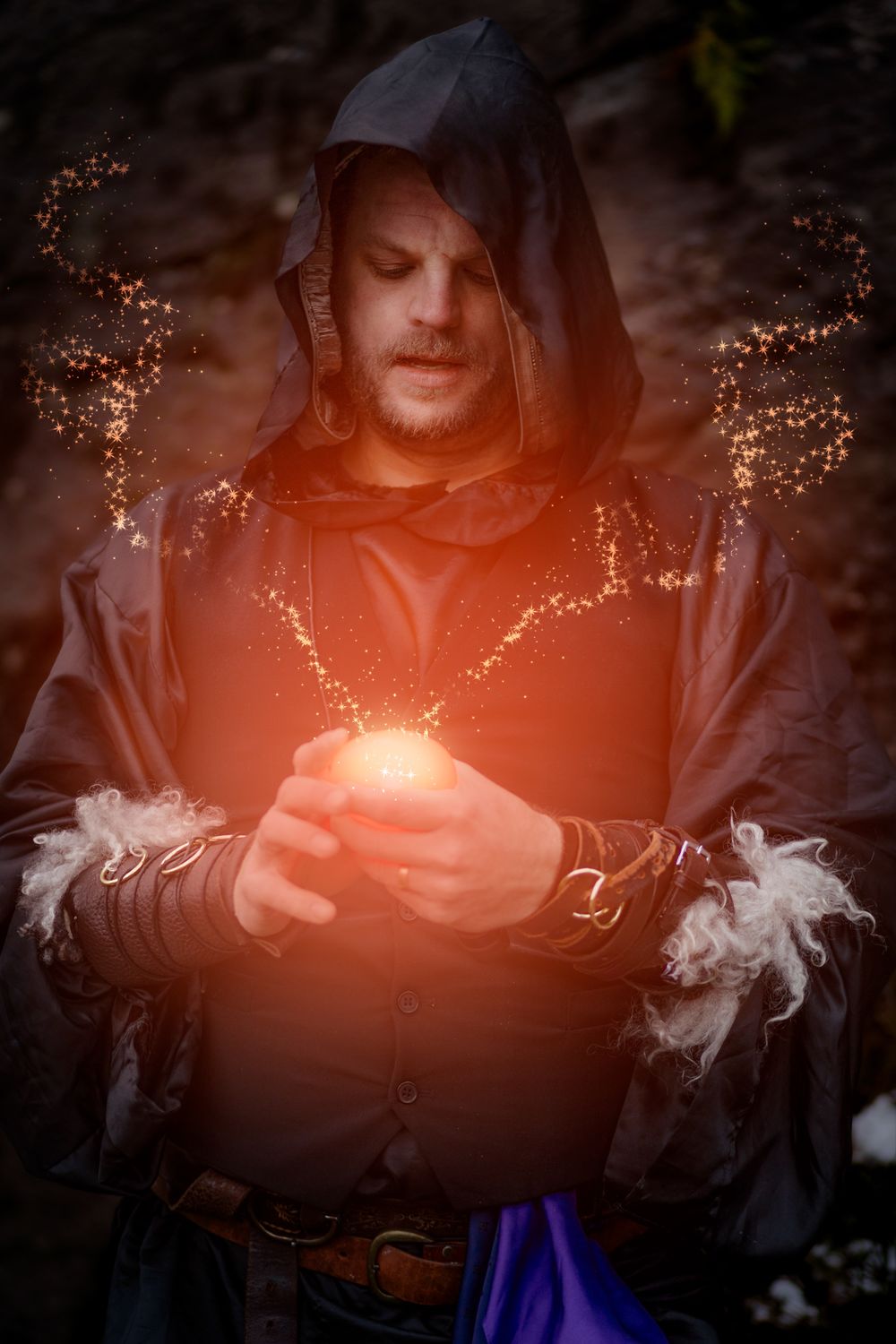 A person holds glowing magical lights in their hands creating an ethereal effect against a dark background.