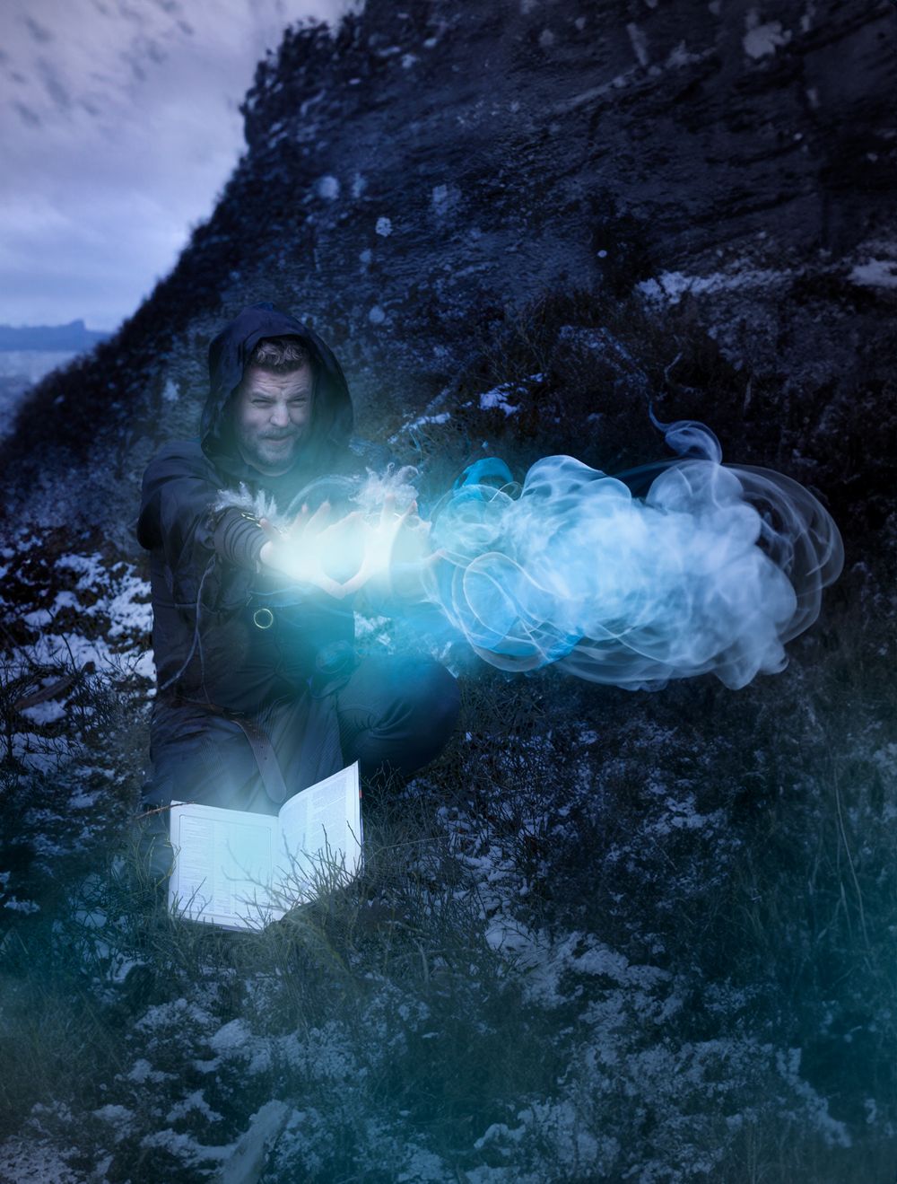 Glowing blue magical energy effect trails through a dark rocky landscape in a fantasy-themed composite photograph.