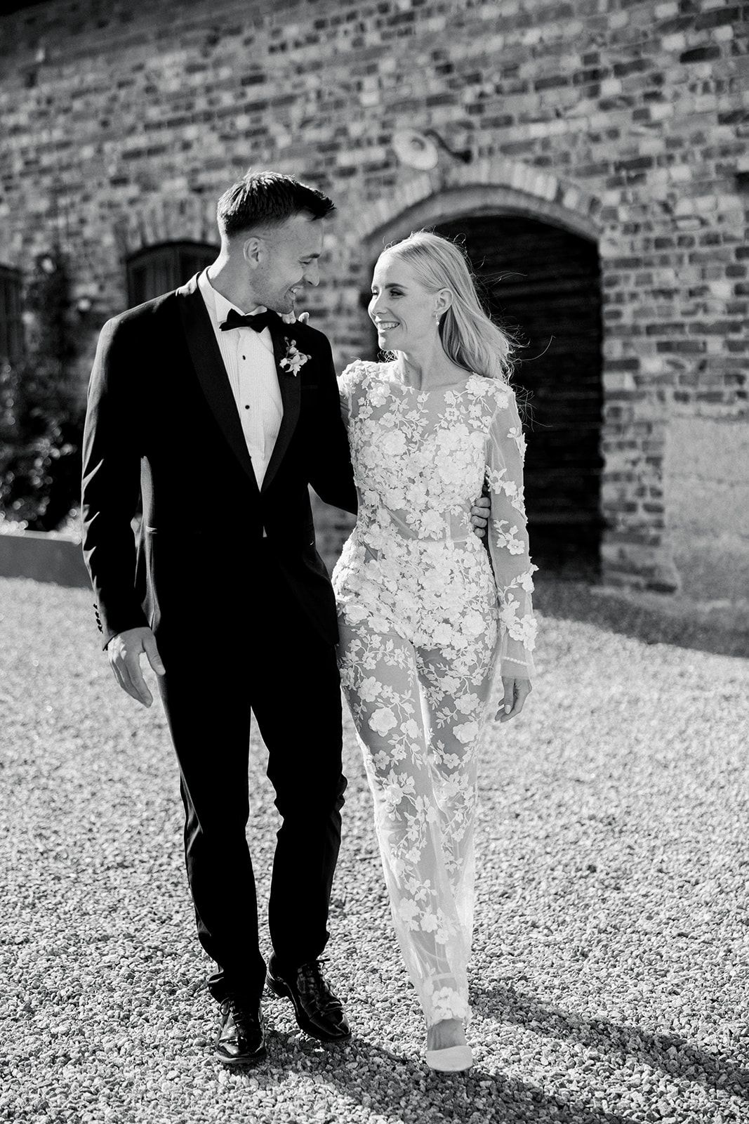 Black and white photo series showing a couple walking together on gravel path against brick wall background.