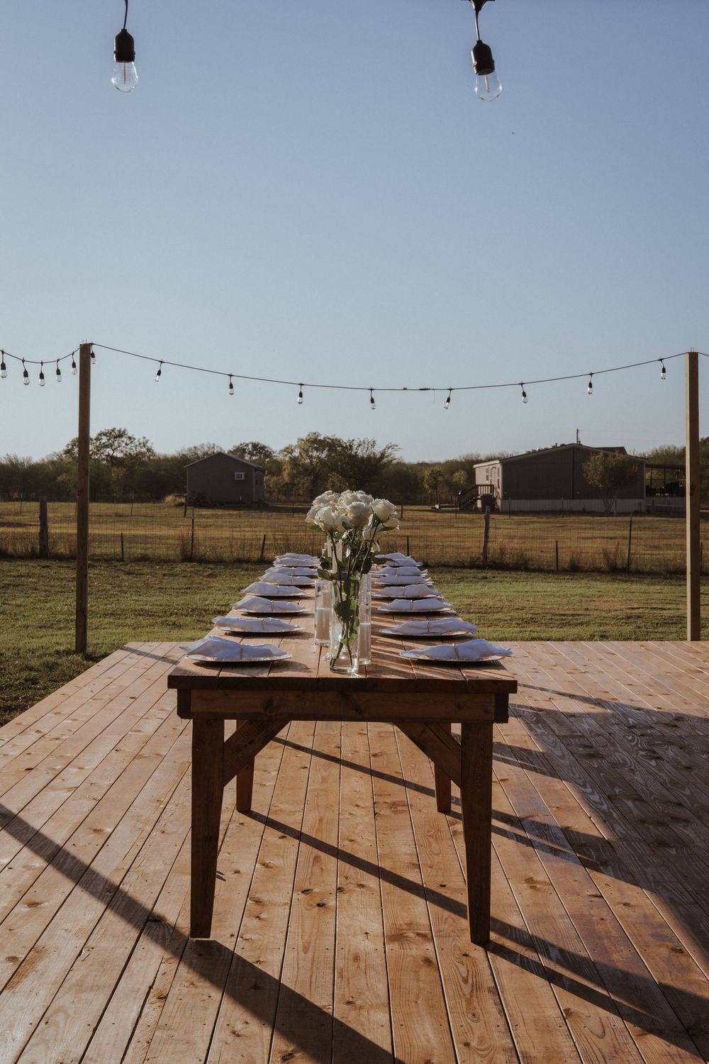 Wooden deck with string lights and floral arrangements set up for an outdoor event.