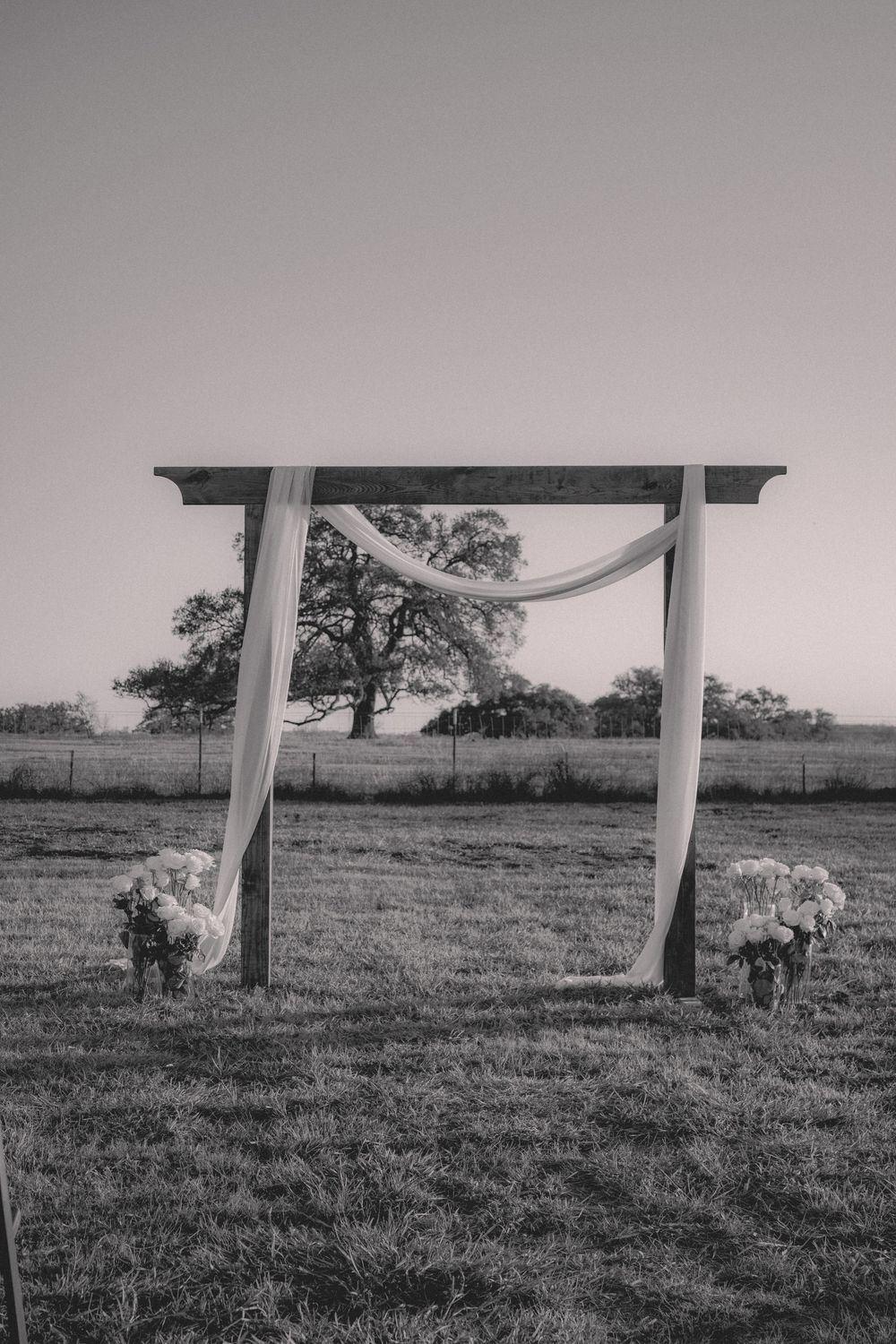 Black and white view of a wedding arch setup in an open field.