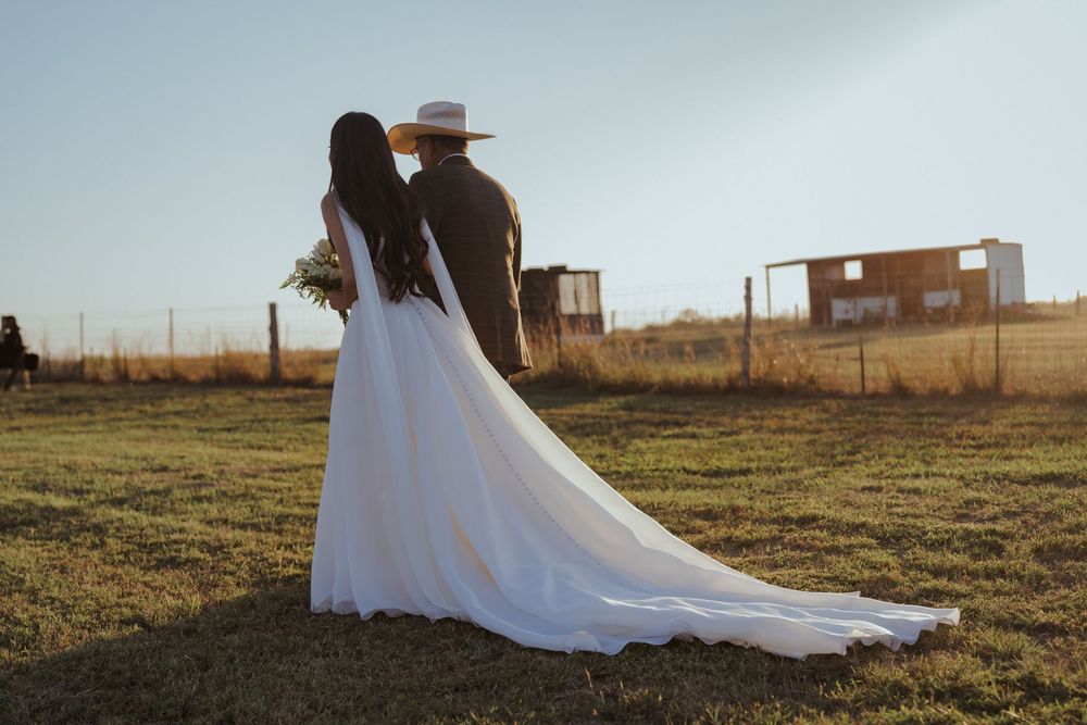 Elegant outdoor wedding with flowing white dress against pastoral farm backdrop at golden hour.