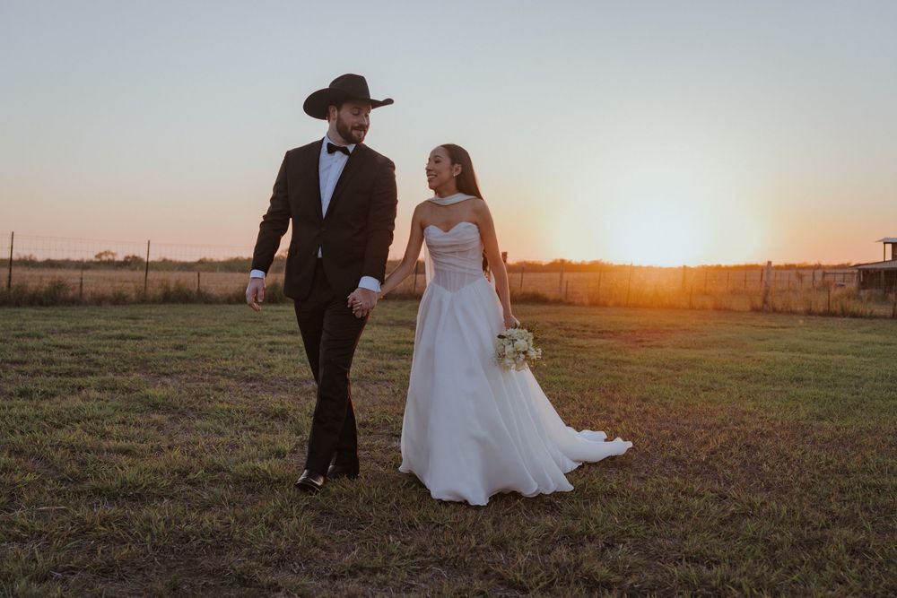 Couple walking through a rustic field at sunset with warm golden light creating a romantic silhouette.