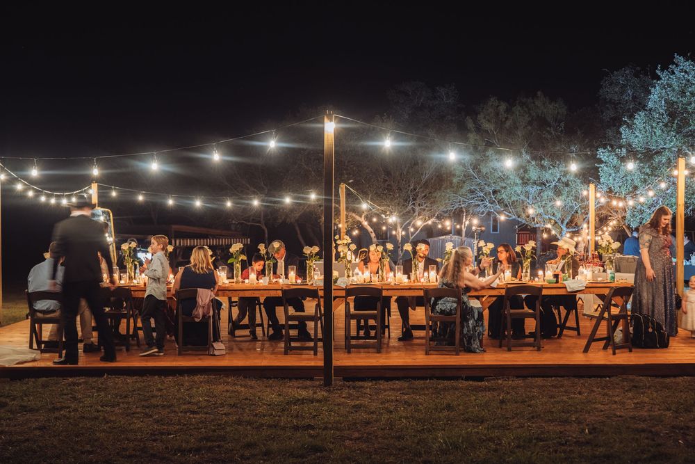 An outdoor evening reception with string lights illuminating long dining tables.