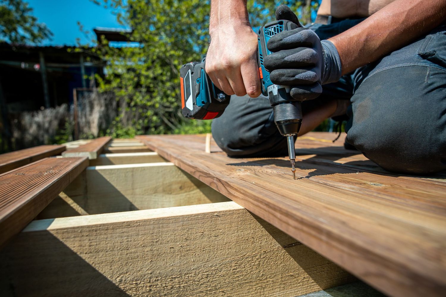 Hands using a circular saw to cut precise lines in wooden decking boards during an outdoor construction project.