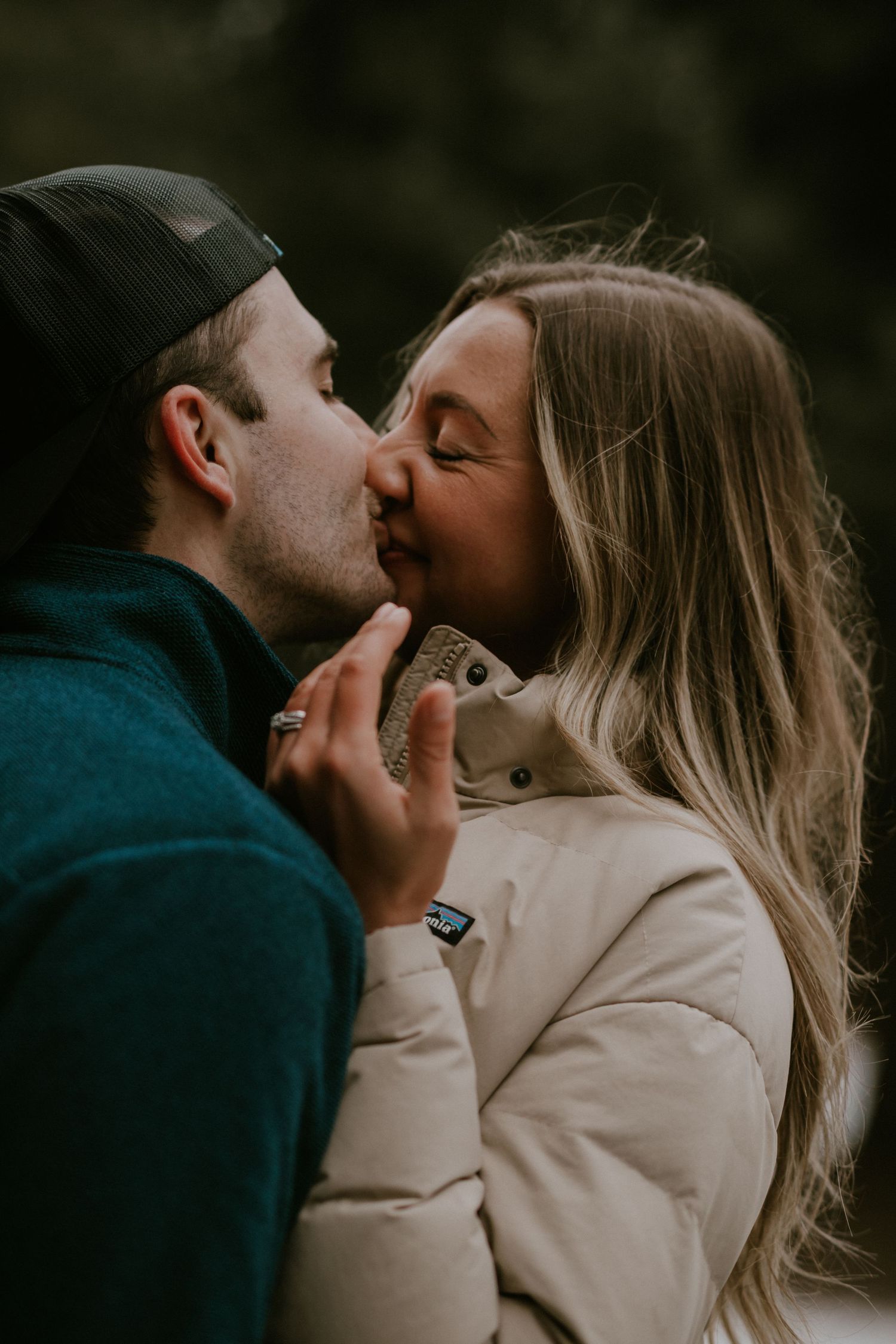 A romantic couple sharing an intimate kiss in moody lighting while wearing casual winter clothing.