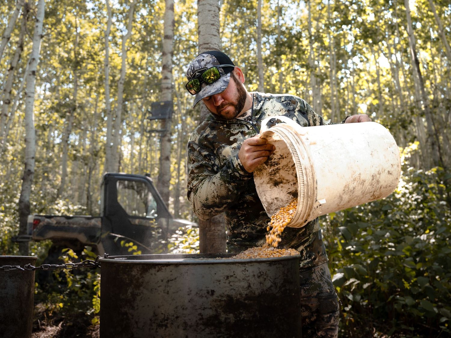 A hunter in camouflage gear felling a tree with an axe in a sunlit aspen forest.
