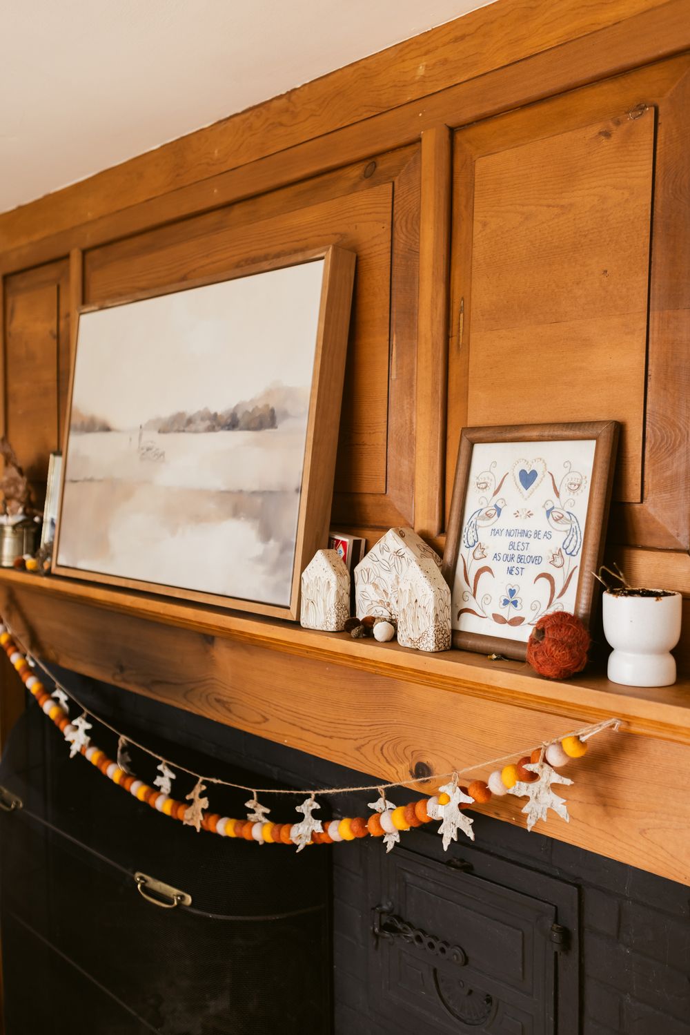 A wooden mantle with a shelf and farmhouse decor and autumn garland hangs in a home in Harvard, Massachusetts