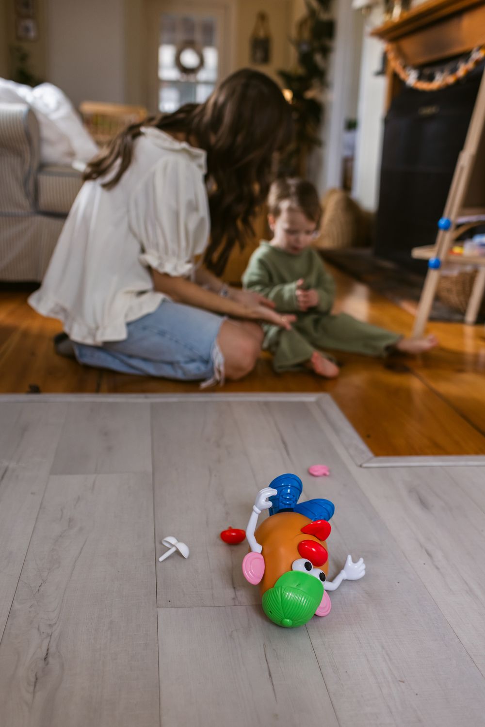 Mr. Potato Head lays on a floor in front of a toddler boy and his mother playing on the floor during a motherhood in-home lifestyle shoot.