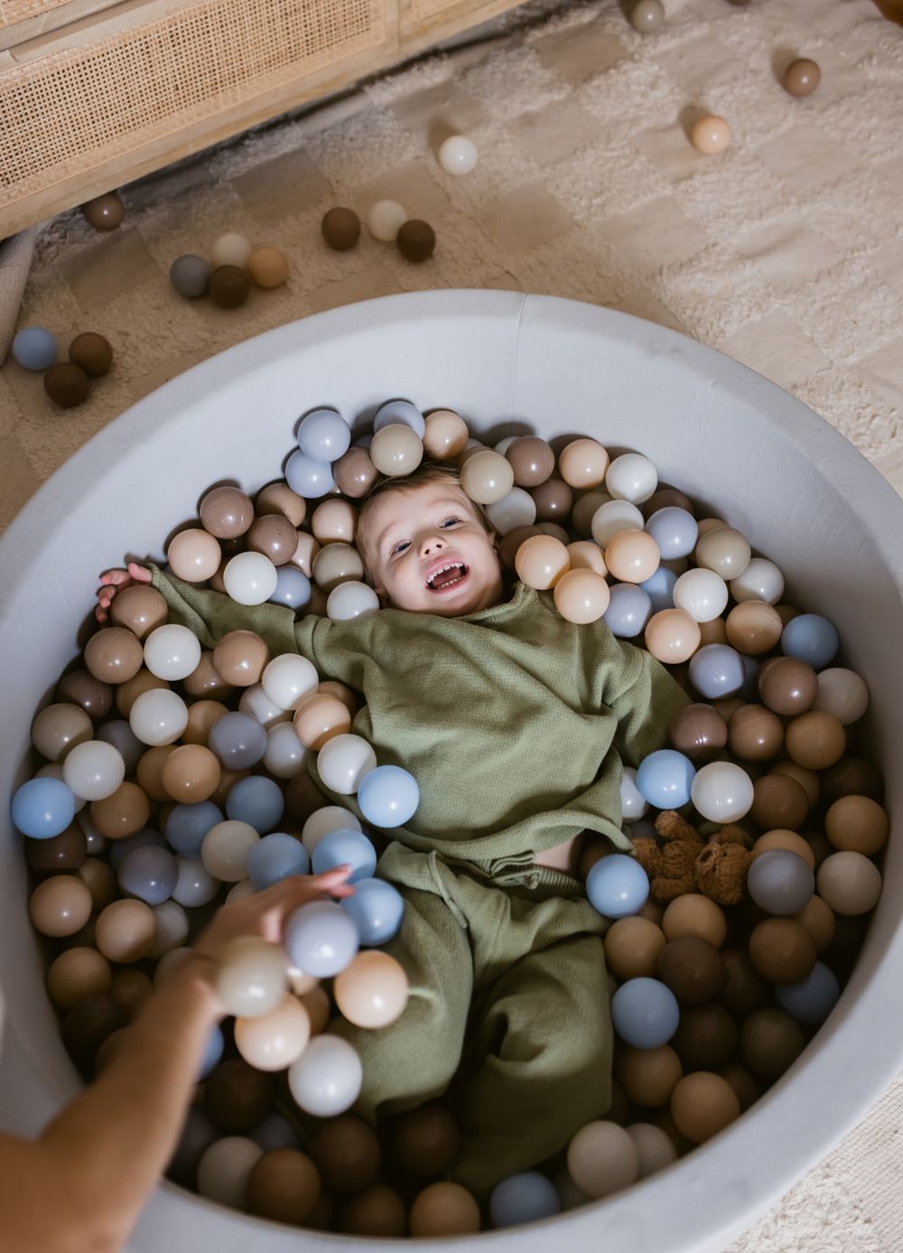 Toddler boy with blue eyes and blond hair plays in his foam ball pit in his bedroom for a Mommy and Me photo session in Harvard, MA