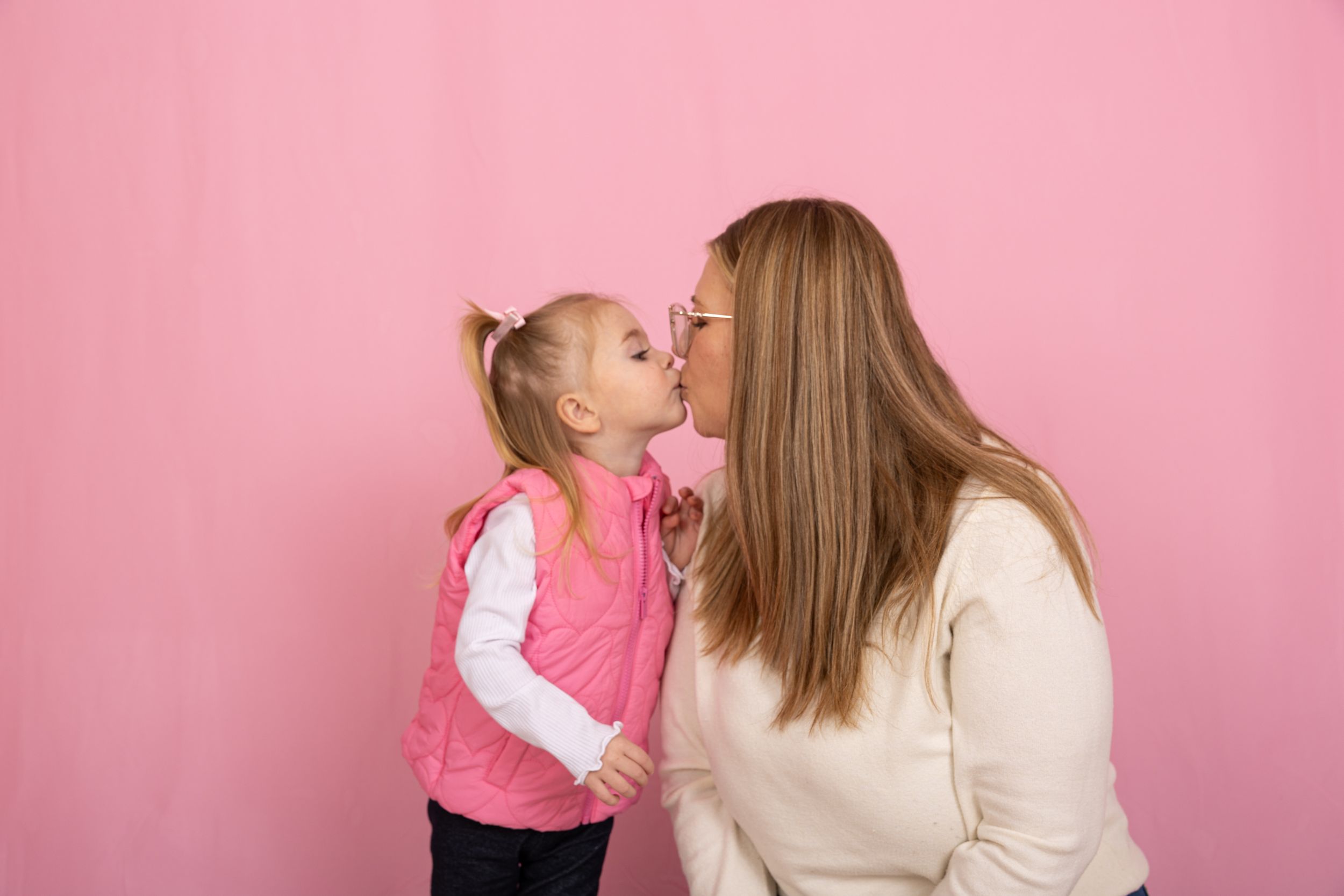 Parent and child in matching cream and pink outfits share playful moment.