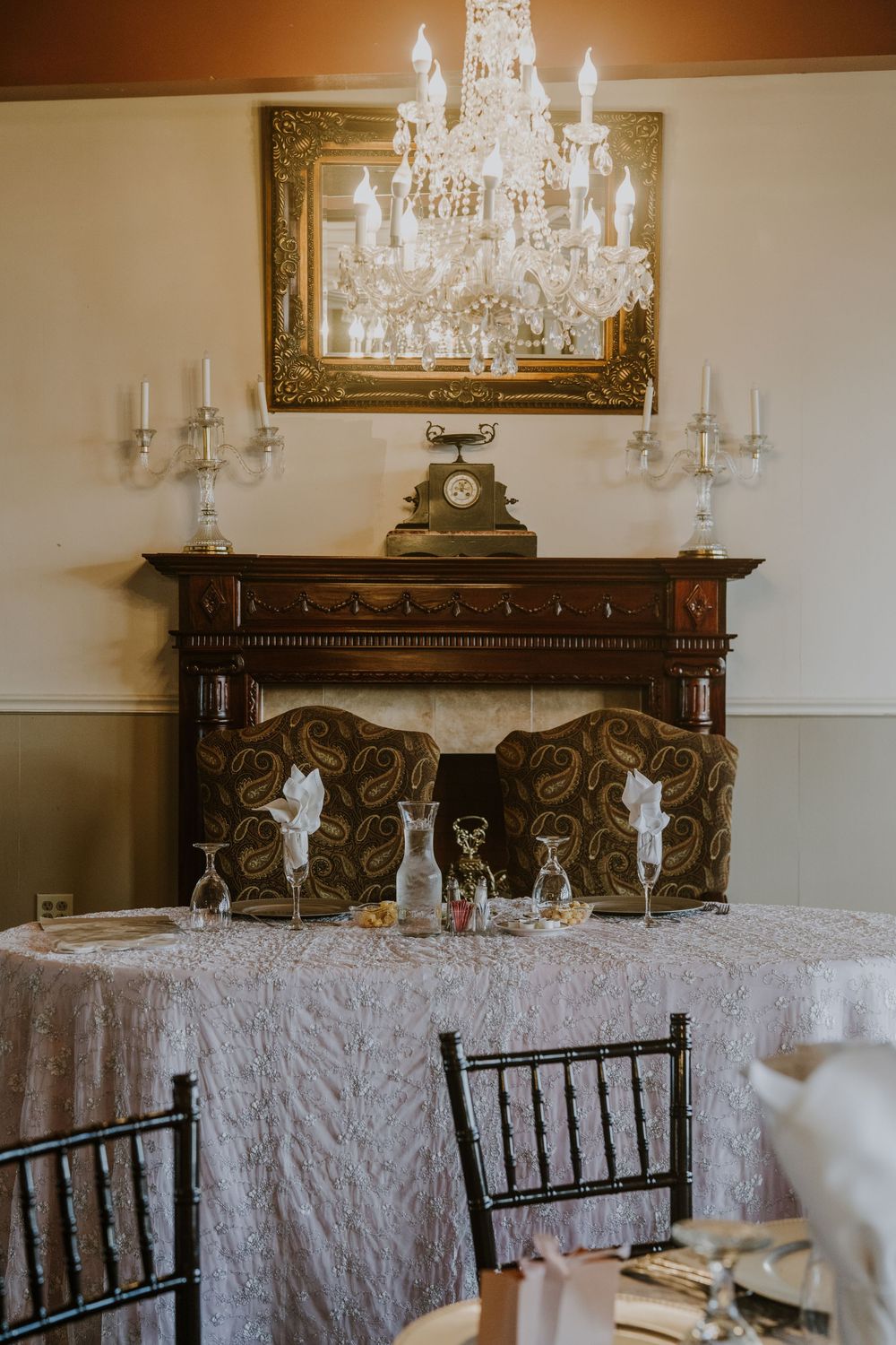 Elegant wedding reception table setup with crystal chandeliers and ornate carved wood furniture.