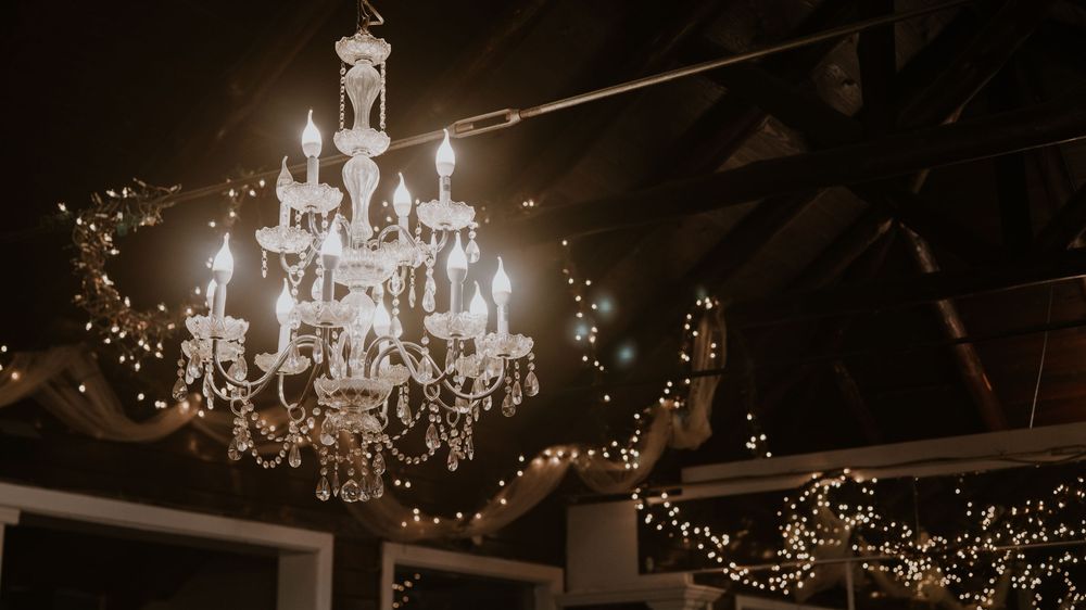 Crystal chandeliers and string lights create a romantic ambiance in an elegant reception venue.