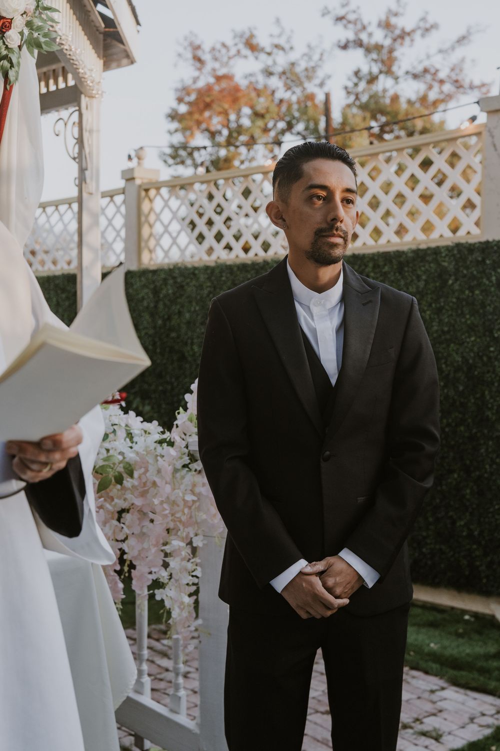Outdoor wedding ceremony with white lattice backdrop and autumn foliage.