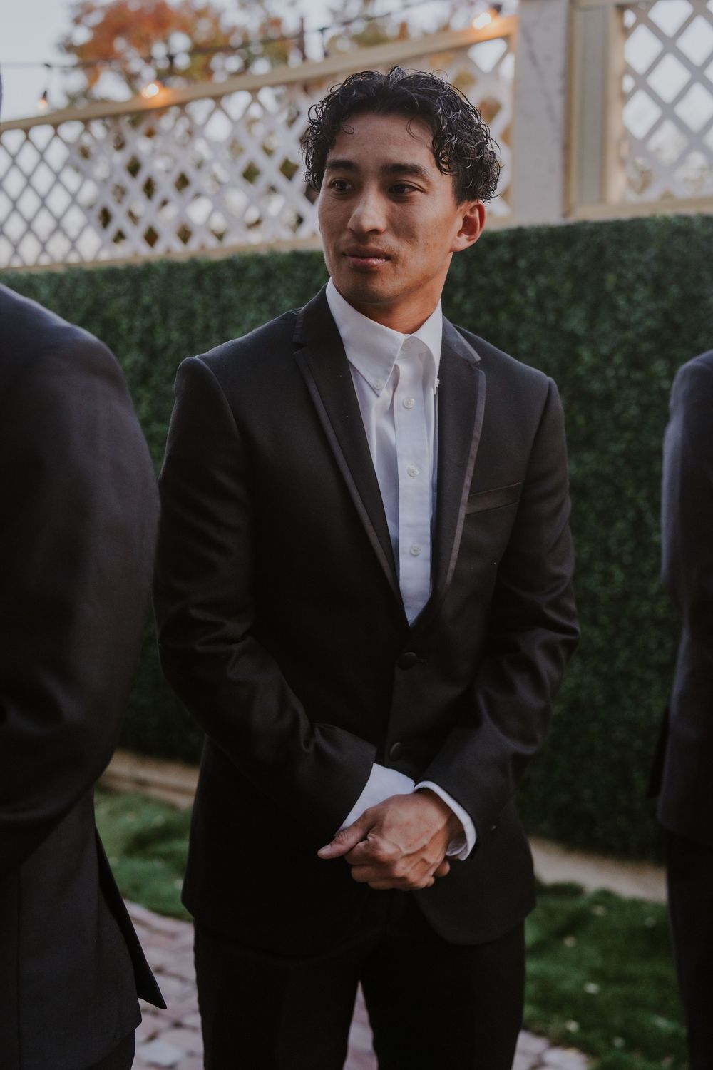 Close-up details of a groom in a black tuxedo and white shirt at an outdoor wedding venue.