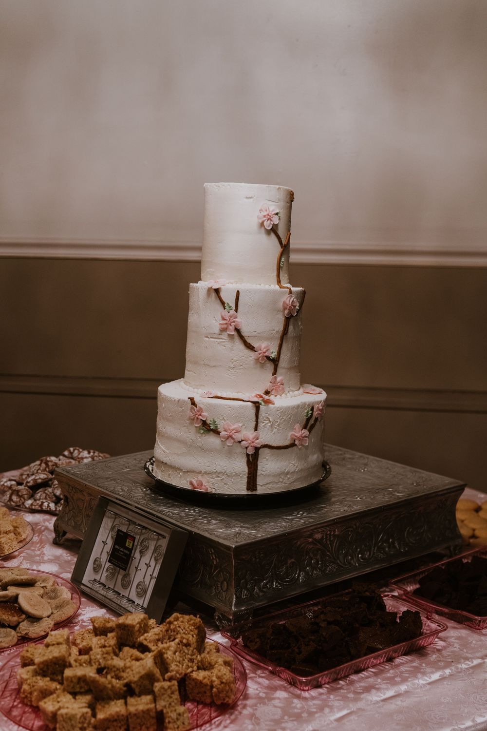 White wedding cake with delicate cherry blossom branch decorations displayed on ornate stand.