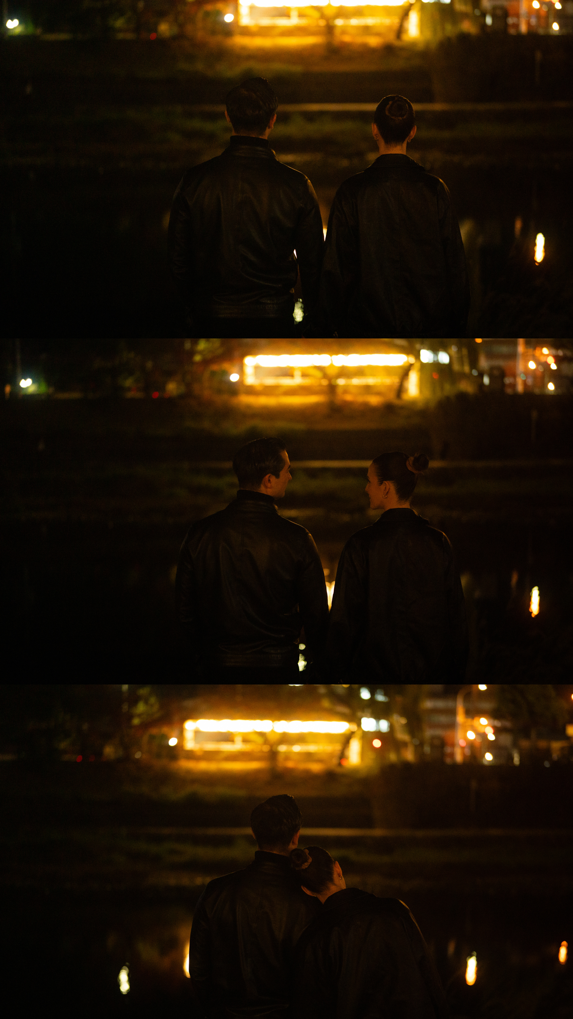A couple stands together by a reflective waterway surrounded by warm golden city lights at night.